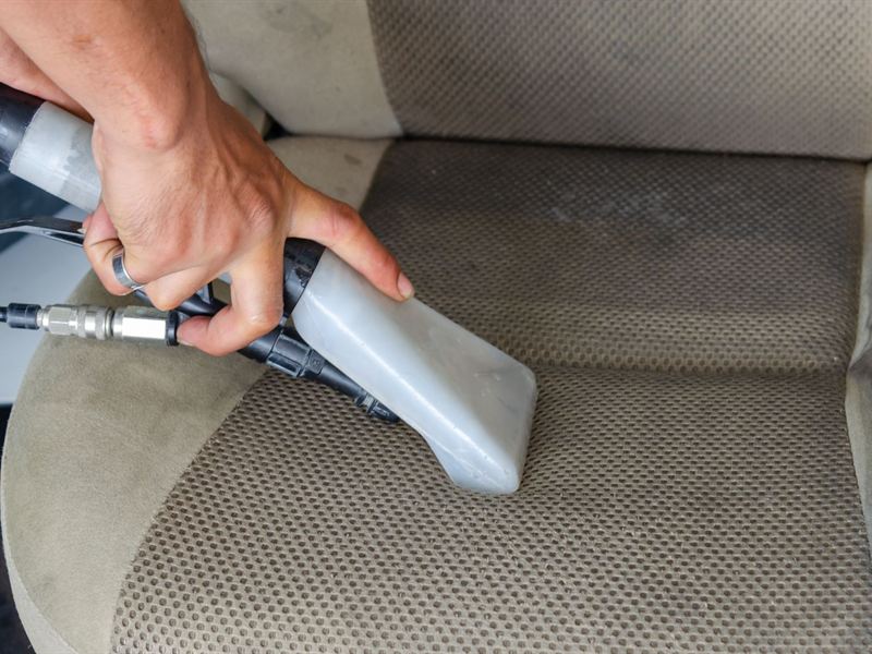 Hands pulling a hot water extraction wand across a fabric car seat