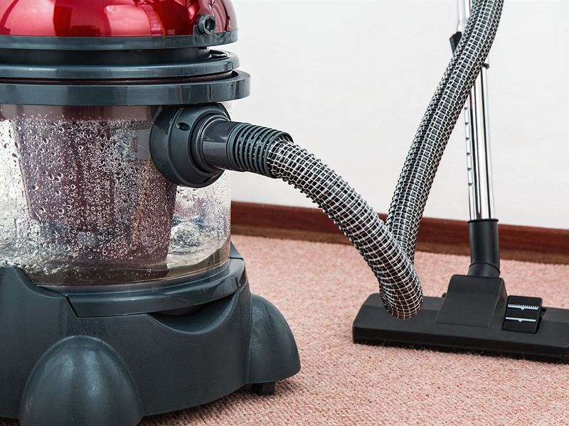 A carpet extractor with a clear recovery tank and upright wand standing on beige carpet