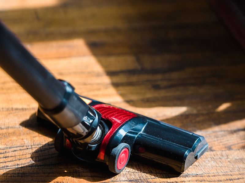A powered floor cleaning head and hose on a wide-plank hardwood floor in afternoon sun