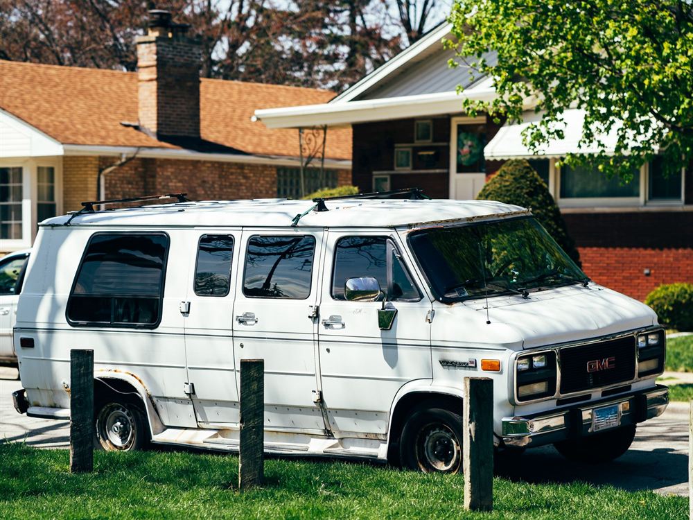 A white panel van with blank side panels parked on a suburban residential street
